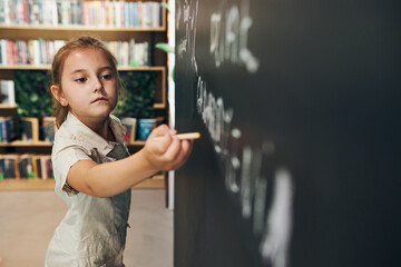 Fototapeta na wymiar Little girl writing on blackboard. Smart student put solve on chalkboard. Back to school. Child having class. Schoolgirl learning at primary school