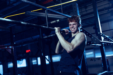 Portrait of sportive muscular young man training, doing pull up exrcises isolated over gym background. Developing strength.