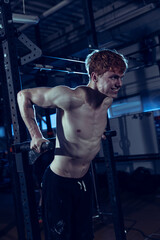 Fototapeta na wymiar Portrait of young muscular man training, doing pull up exercises isolated over gym background. Developing strength. Body texture