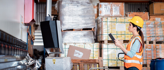 Asian woman auditor work looking up stocktaking inventory in warehouse she using tablet with wide...