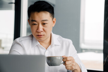 Adult asian businessman working on laptop at desk in office