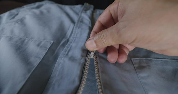 Closeup shot of unzip the jacket while the camera follows the man's hand. 
