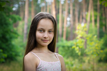 Portrait of beautiful preteen smiling girl in forest with pine-trees on summer sunset day