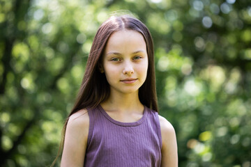 Portrait of beautiful preteen smiling girl in forest on summer sunny day