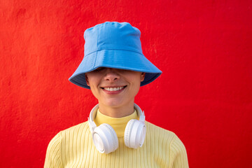 Smiling woman with headphones and blue bucket hat in front of red wall
