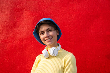 Smiling woman with headphones and bucket hat in front of red wall