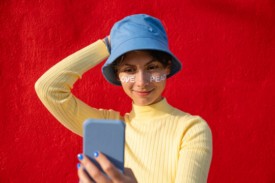 Woman with bucket hat taking selfie on smart phone in front of red wall
