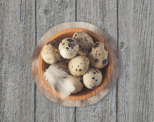 Quail eggs in a plate centered on a textured table with a round napkin under the plate and a small feather.
