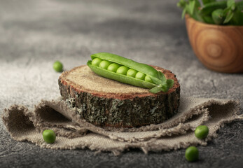 Green peas lying on a wooden stand on a linen napkin on a gray textured table.