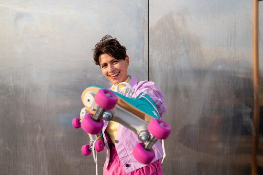 Happy woman holding roller skates by wall