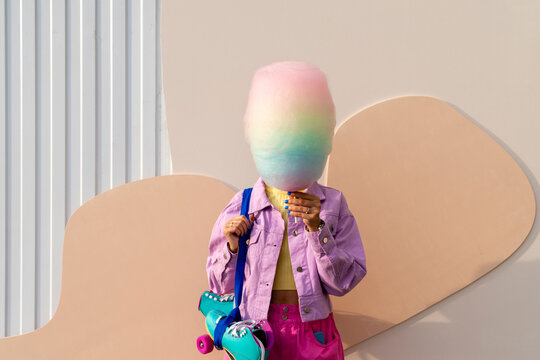 Woman covering face with cotton candy in front of wall