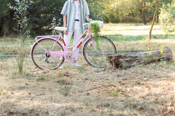 Fototapeta premium Cropped side view of unrecognizable young fashinable man holding a pink bicycle with a wicker basket and plants