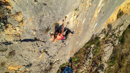 AERIAL: View of young sporty woman lead climbing up the gorgeous limestone wall