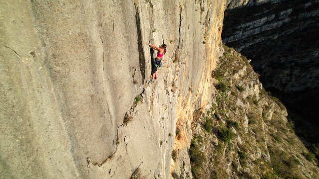 AERIAL: Female climber ascending up the rock wall and searching for good grips