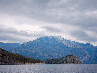 travel to Lagoon in Oludeniz, Fethiye, Turkey. beach near Darbogaz. with view to Mount Babadag, Winter landscape with mountains, green forest, azure water, beach and cloudy sky