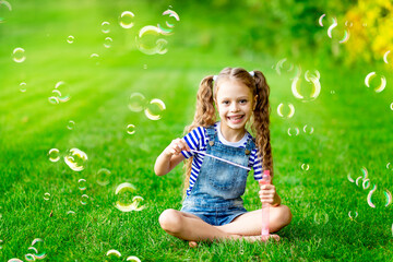 funny baby girl in the summer on the lawn with soap bubbles on the green grass, having fun and rejoicing, space for text