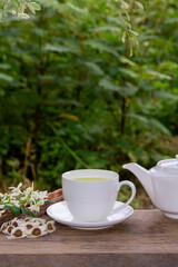 Moringa Tea in white cup and fresh green leaf, flower, pod and seeds with teapot on wooden, blur background. 