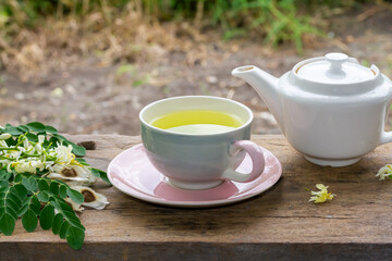Obraz na płótnie Canvas Moringa Tea in cup and fresh green leaf, flower and seeds with teapot on wooden, blur background. Moringa oleifera tropical herb healthy lifestyle concept.