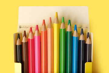 Multicolored pencils in a box isolated on yellow.