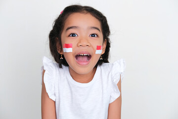 Closeup portrait of indonesia kid wearing country flag stickers in her cheeks showing cheerful...