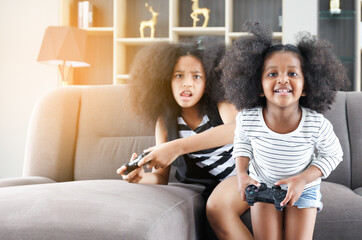 Obraz premium Black sister and cute African American woman having fun holding game joystick sitting on the sofa