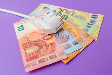 Electric plug,euro paper money banknotes.Purple indoors background. Increasing of electricity cost for all residential and business users, expensive energy bill and rise in electricity prices concept.