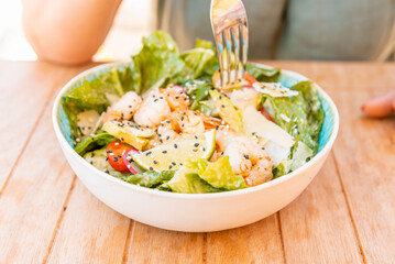 Healthy salad plate. Part woman hand and fork.Fresh summer salad with shrimp, avocado and tomato in bowl on light table. Grilled shrimps and fresh vegetable salad.Healthy food.