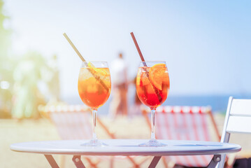 Two glasses of orange spritz aperol drink cocktail on table outdoors with sea and trees sunrise...