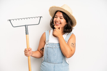 hispanic pretty girl feeling shocked,laughing and celebrating success. farmer and rake concept