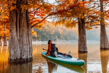 Woman smile and relax on stand up paddle board at the lake between Taxodium trees in autumnal season
