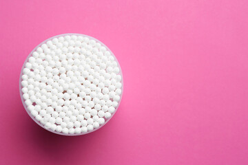 Many cotton buds in container on pink background, top view. Space for text