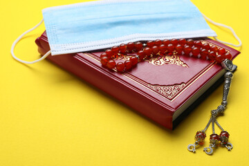 Muslim prayer beads, Quran and medical mask on yellow background, closeup
