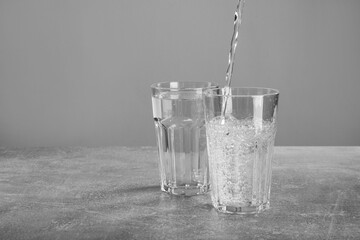 Pouring soda water into glass on grey table. Space for text