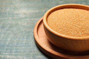 Brown sugar in bowl on light blue wooden table, closeup. Space for text