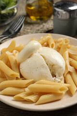 Plate of delicious pasta with burrata on wooden table, closeup
