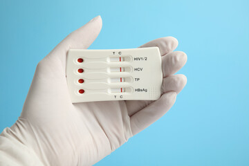 Fototapeta na wymiar Doctor holding disposable express test for hepatitis on light blue background, closeup