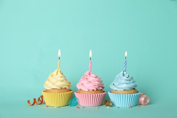 Delicious birthday cupcakes with burning candles, sprinkles and streamers on turquoise background