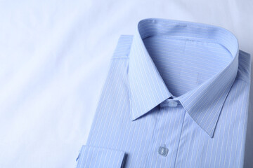 Stylish light blue shirt on white fabric, closeup. Dry-cleaning service