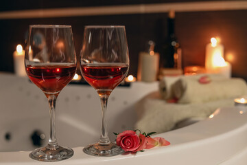 Wine in glasses and rose on edge of bath indoors. Romantic atmosphere