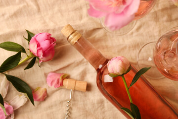 Flat lay composition with rose wine and beautiful peonies on beige fabric