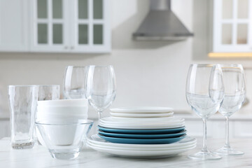 Different clean dishware and glasses on white marble table in kitchen