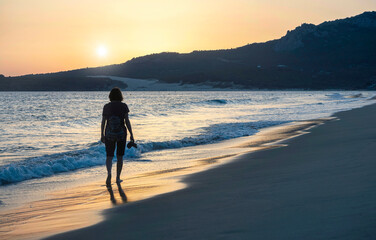 Naklejka premium Beautiful seascape. Unrecognizable woman walking at sunset on the seashore. Silhouette of woman.