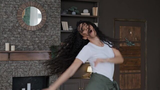 Expressive emotional young woman dancing sensual moving dynamic to music female professional dancer rehearsing dance at home shaking long curly hair spinning enjoying weekend alone excited girl dances