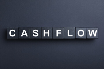 Wooden cubes with phrase Cash FLow on black background, flat lay