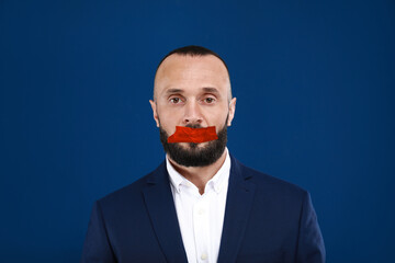 Mature man with taped mouth on blue background. Speech censorship
