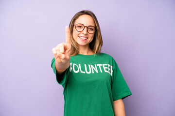 pretty caucasian woman smiling and looking friendly, showing number one. volunteer concept