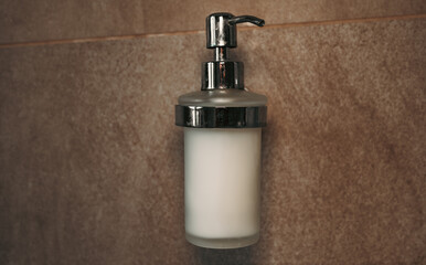 Fototapeta na wymiar liquid soap isolated on bathroom wall. push-button liquid soap. close up of a silver push button