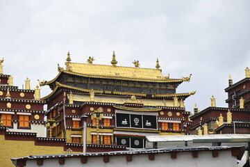 Naklejka premium The colorful rooflines of the buildings at the Songzanlin monastery in Shangri-La, China - contrasting against the clear blue sky and adorned with many flags