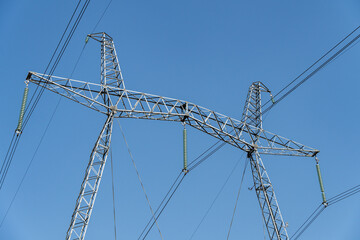 Fototapeta premium Fragment of metal pole of high-voltage power line VL-750 kV against blue sky. Close-up. There are more than 20 insulators in garland. Garlands of insulators are made of glass.