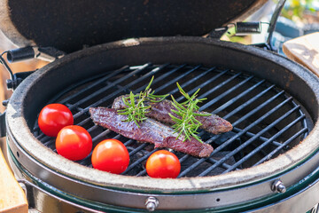 the raw red tenderloin from a chamois on a charcoal grill with twigs from rosemary and cherry tomatoes is ready for outdoor grilling